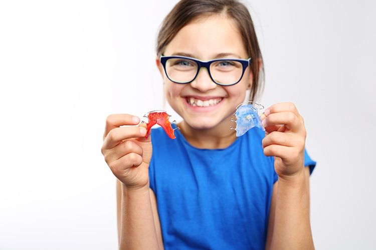 A child holding two colorful Hawley retainers